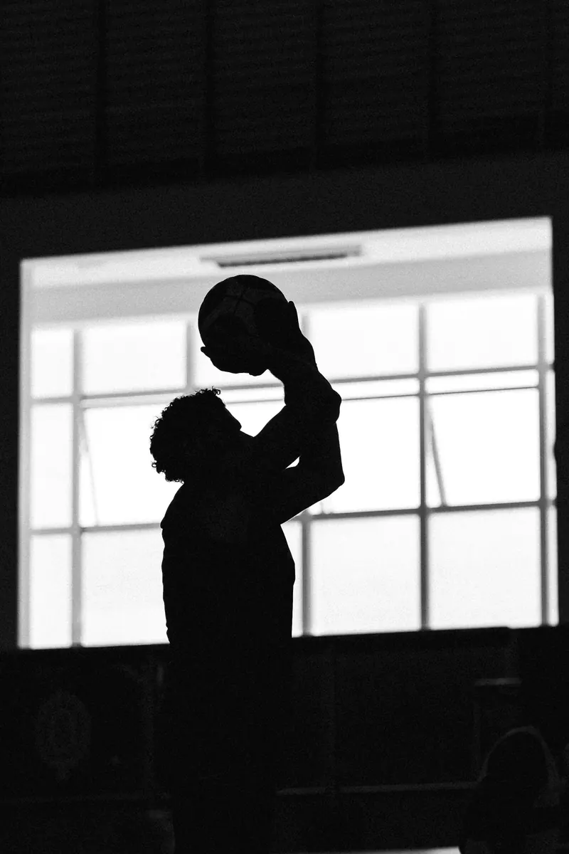 Black and white silhouette of a player shooting against a gym window